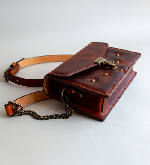 A brown leather handbag with a unique crackling effect and antique brass hardware, displayed against a neutral background.