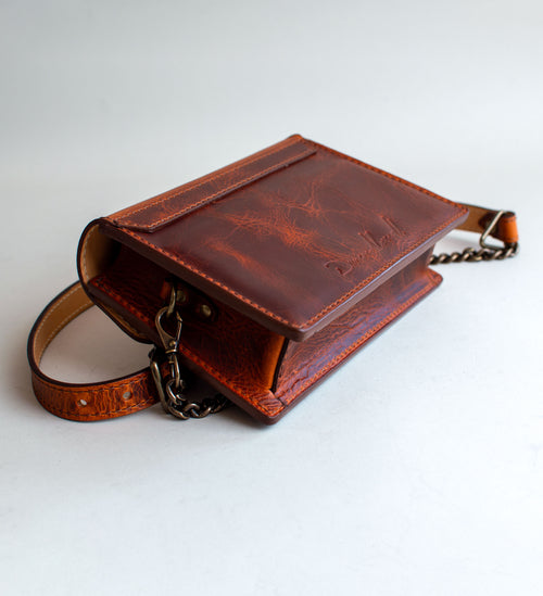 A brown leather handbag with a unique crackling effect and antique brass hardware, displayed against a neutral background.