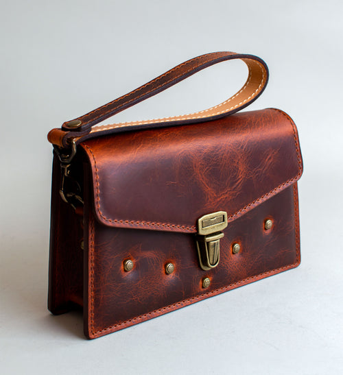 A brown leather handbag with a unique crackling effect and antique brass hardware, displayed against a neutral background.