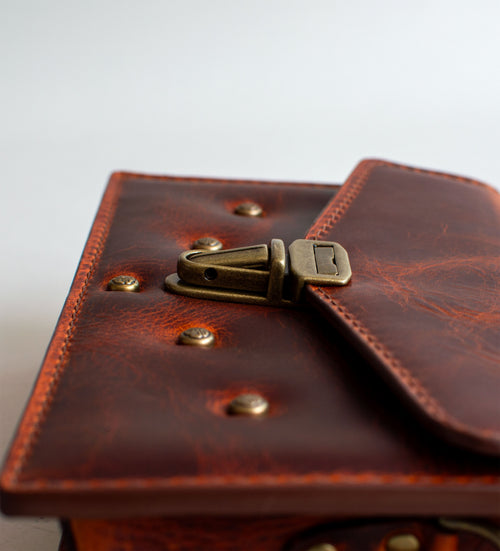 A brown leather handbag with a unique crackling effect and antique brass hardware, displayed against a neutral background.
