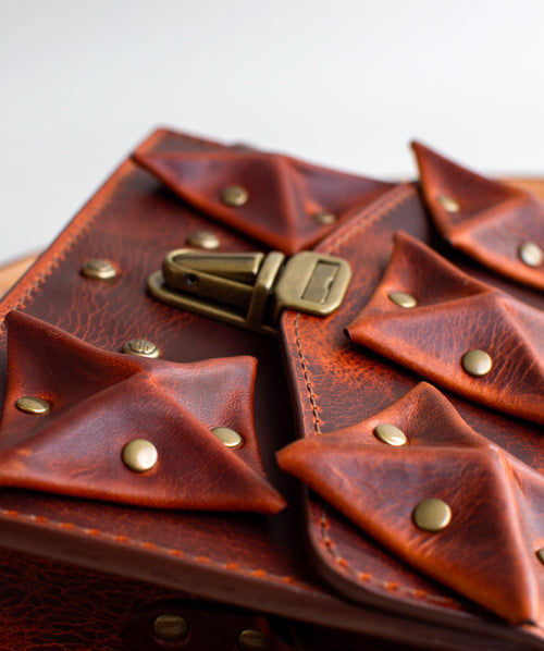 Close-up-View-Of-Amber-Colored-luxury-leather-handbag-with-folded-origami-leather-embellishments-handmade-in-the-us-with-brass-hardware