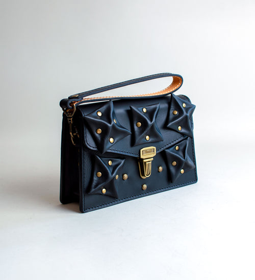 Side-View-Of-Black-Colored-luxury-leather-handbag-with-folded-origami-leather-embellishments-handmade-in-the-us-with-brass-hardware