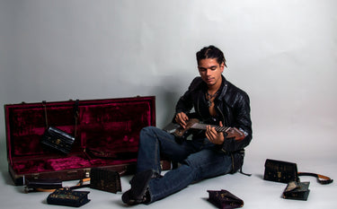 Model playing guitar surrounded by luxury purses and handbags