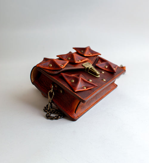 Side-View-Of-Amber-Colored-luxury-leather-handbag-with-folded-origami-leather-embellishments-handmade-in-the-us-with-brass-hardware