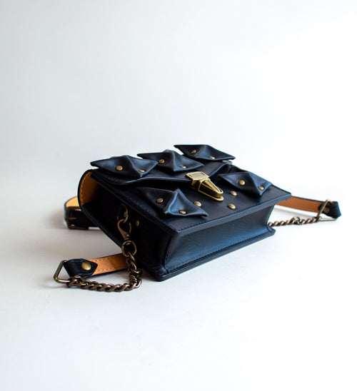 Side-View-Of-Black-Colored-luxury-leather-handbag-with-folded-origami-leather-embellishments-handmade-in-the-us-with-brass-hardware