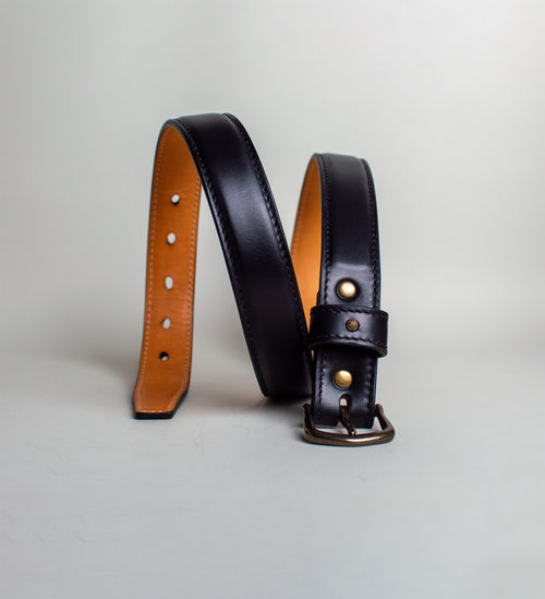 Black and brown leather belts with brass studs on a light gray background