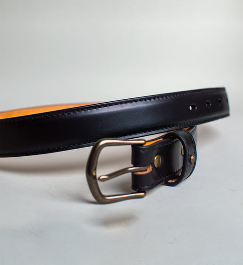 Black leather belt with a gold buckle on a light gray background