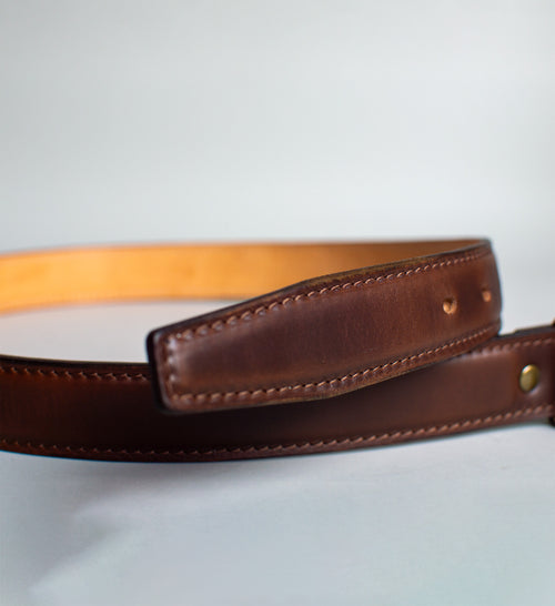 Brown leather belt with a Brass buckle on a light gray background handmade