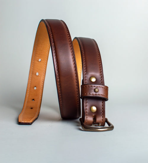 Brown leather belt with gold buckle on a light gray background